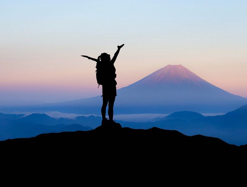 「TOEIC900点を達成したその先に見えた景色」 「富士山を背に山頂で両手を広げる登山者」