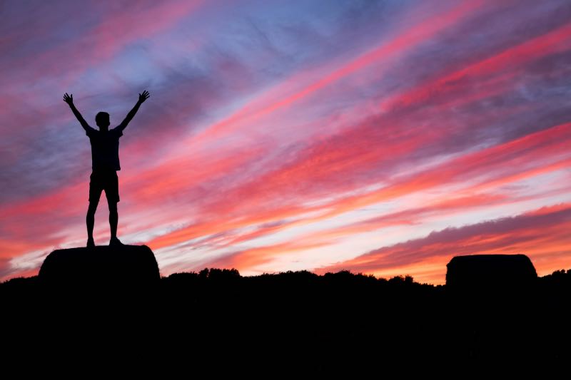 夕焼け空を背に、両手を広げて立つ人のシルエット。英語学習の達成感と自由を象徴する場面