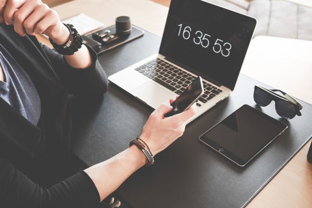 腕時計とスマートフォン、ノートPCのタイマー表示が並ぶデスク｜時間を意識して勉強時間を管理する社会人のイメージ