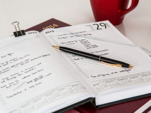 予定がびっしり書き込まれた手帳の上にペンが置かれた写真