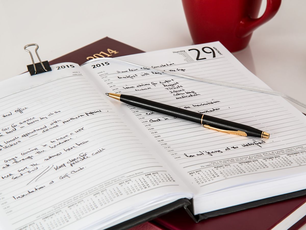 予定がびっしり書き込まれた手帳の上にペンが置かれた写真