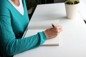 ノートにペンを走らせる女性の手元｜英語日記を書こうとしているイメージ
