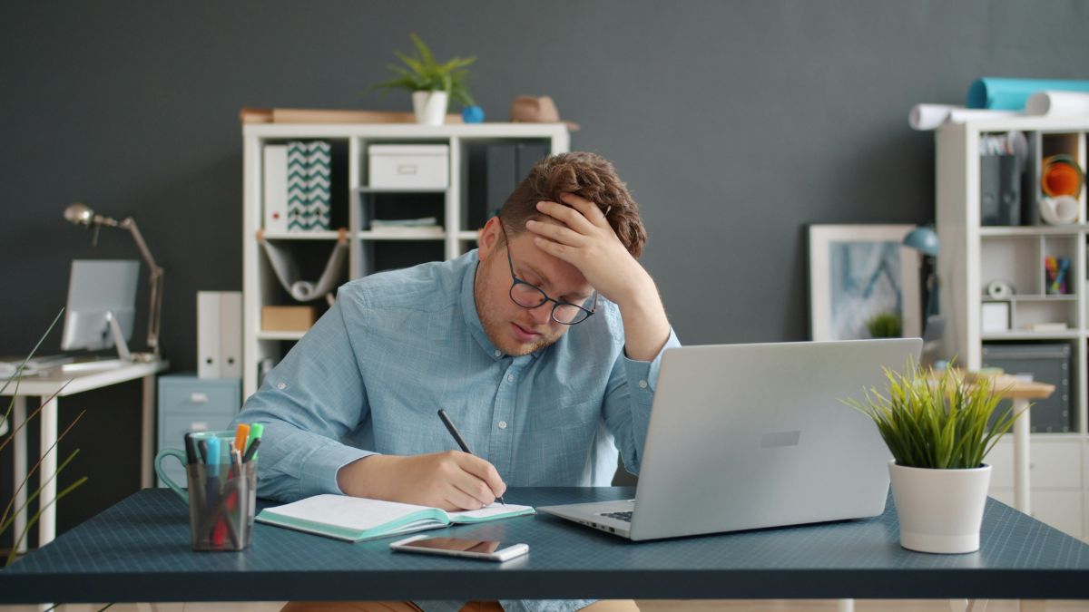 デスクでノートを書きながら頭を抱える男性｜TOEIC Part5攻略に悩む社会人のイメージ