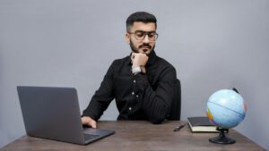 デスクでノートPCを前に顎に手を当てて考え込む男性|TOEIC Part6の解き方を悩む社会人のイメージ