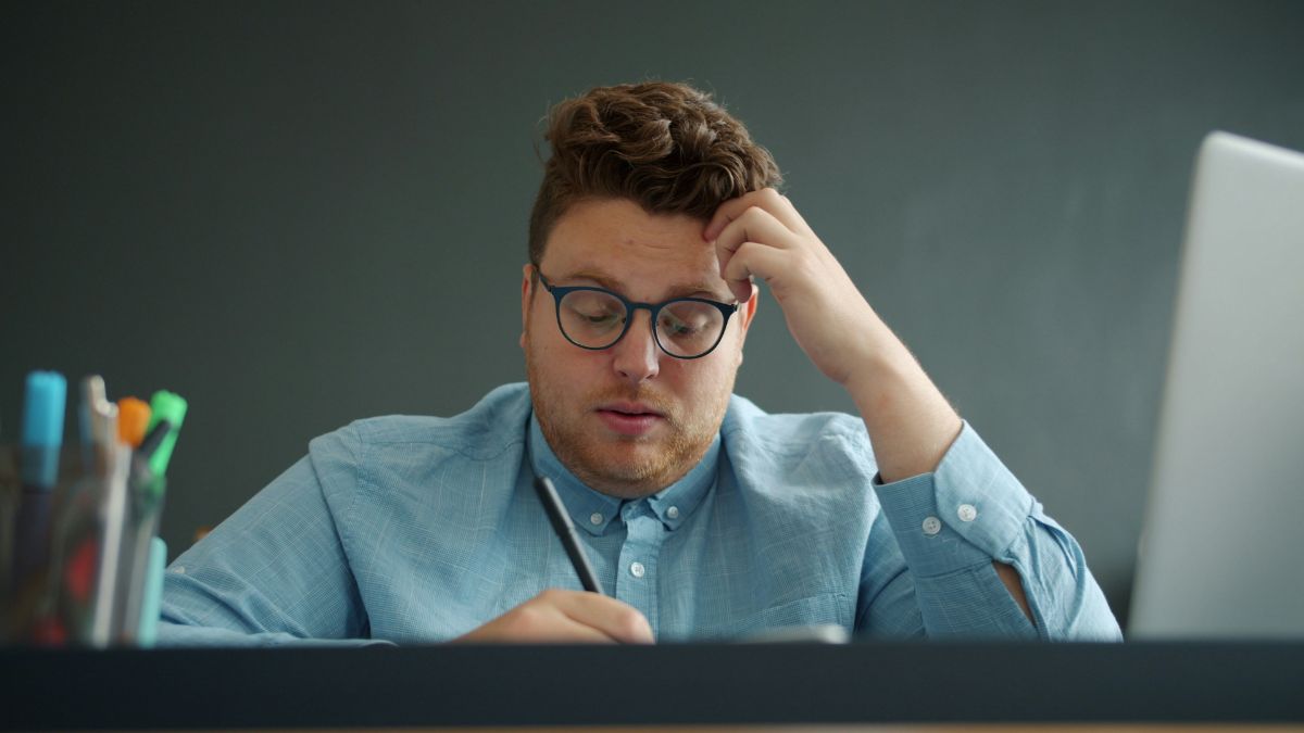 デスクでノートを手に頭を抱えて考え込む男性｜TOEIC記事文の読みにくさに悩む社会人のイメージ