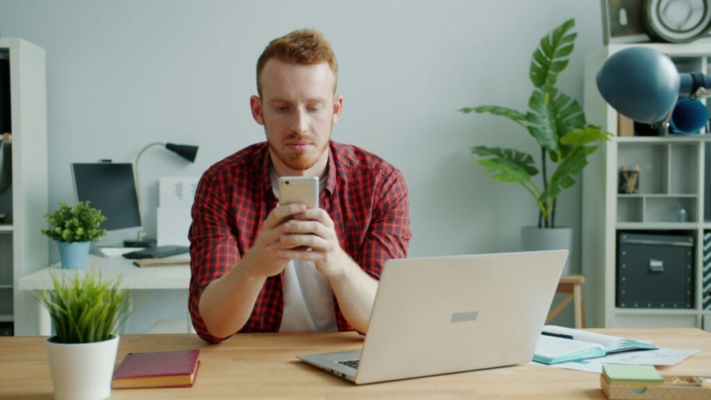 デスクでスマートフォンの英語ニュースを真剣に読む男性