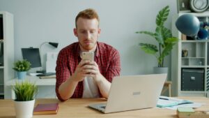 デスクでスマートフォンの英語ニュースを真剣に読む男性