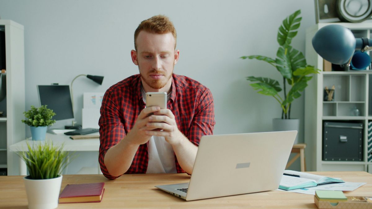 デスクでスマートフォンの英語ニュースを真剣に読む男性