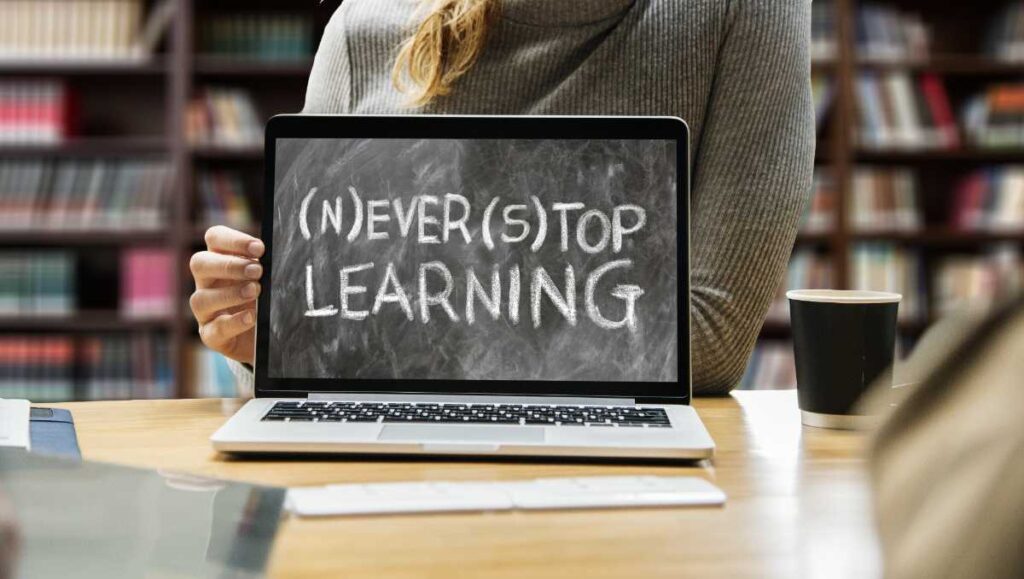 「Never Stop Learning」と書かれたノートPCを持つ手元