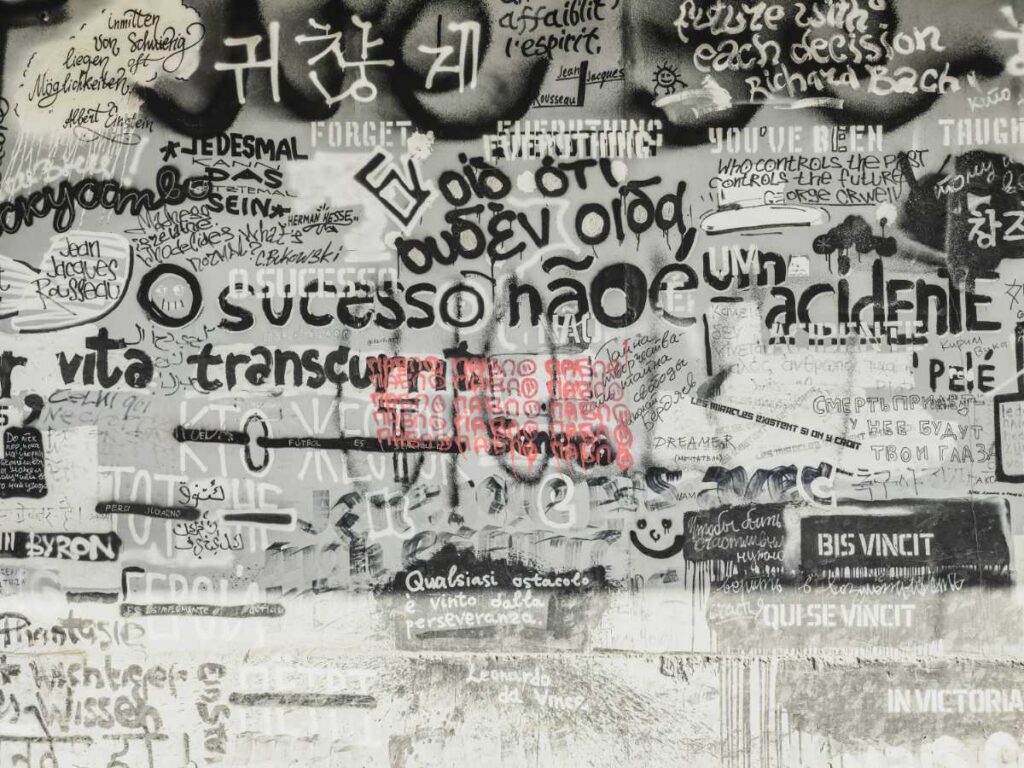多言語の文字が重なり合う壁の写真｜言葉が持つ「記号」と「イミ」の多様性を象徴する一枚