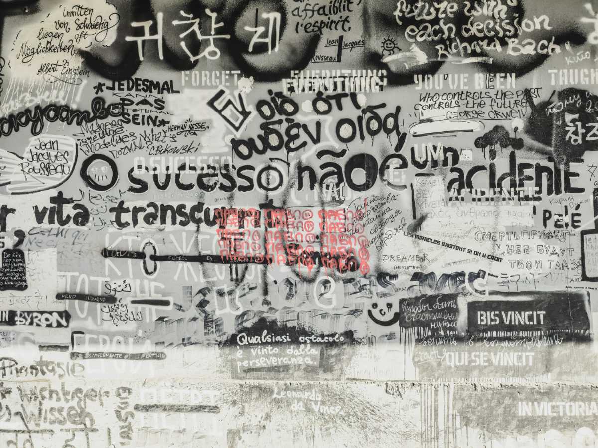 多言語の文字が重なり合う壁の写真｜言葉が持つ「記号」と「イミ」の多様性を象徴する一枚